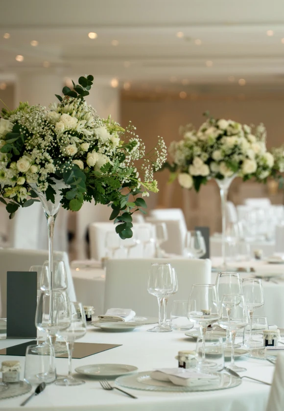 Elegante allestimento da pranzo all'interno della Sala Ricevimenti con alte composizioni floreali e bicchieri pregiati su tovaglie bianche, che creano un'atmosfera romantica.