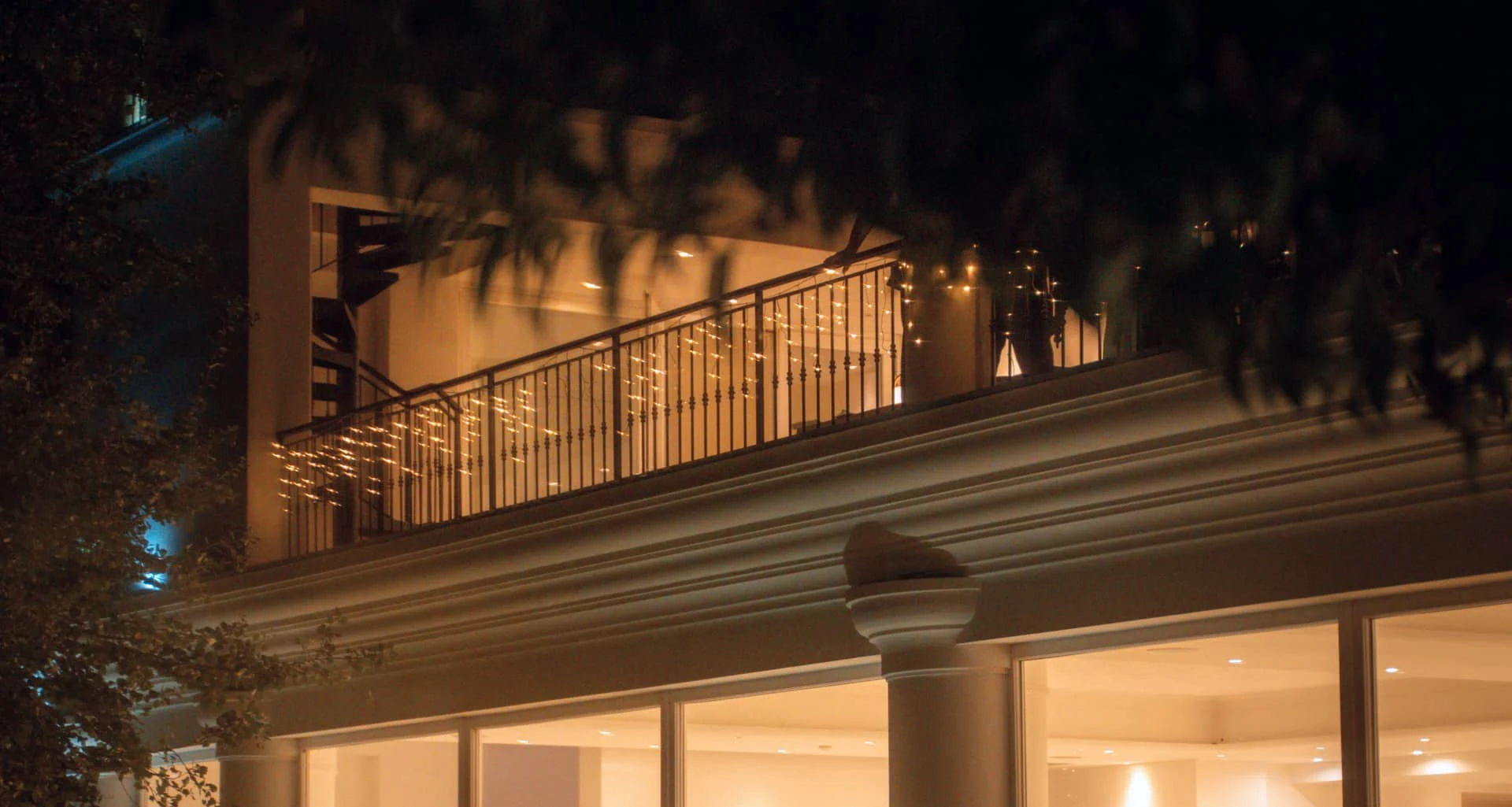 Una vista accogliente del lato della sala ricevimenti di notte, con luci a catena, parzialmente oscurate dai rami degli alberi.