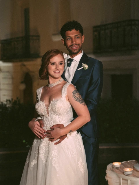 Gli sposi posano insieme in abiti nuziali. Lo sposo sta dietro la sposa con le mani sulla sua vita.